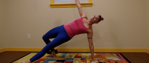 Image of Coach Ren wearing bright athletic apparel and performing a Turkish Get-Up in a beige room on a colorful rug.