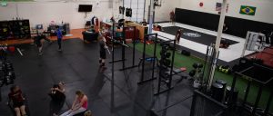 Image of the Seattle gym with large, open mat space showing two small classes, an independent lifter at one of the four squat racks, and a martial arts class taking place on the other side of a net.