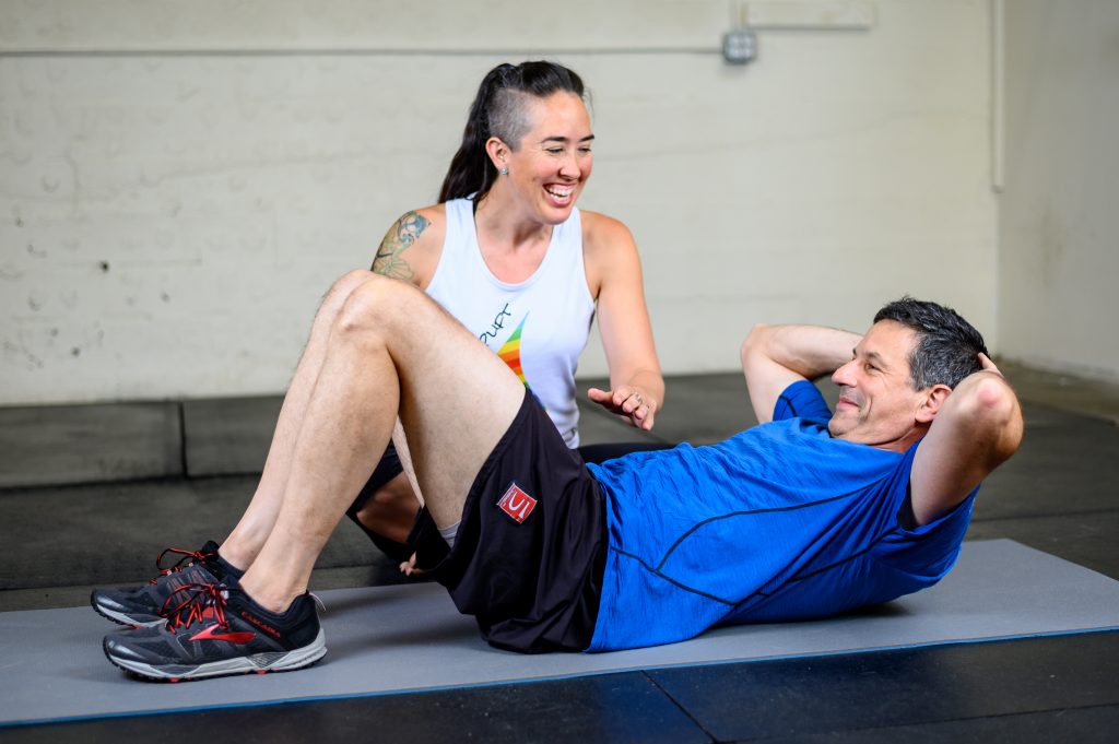 Image of Coach Kira working with a client doing mat Pilates. Both are smiling and laughing as Kira directs the client through the movement.