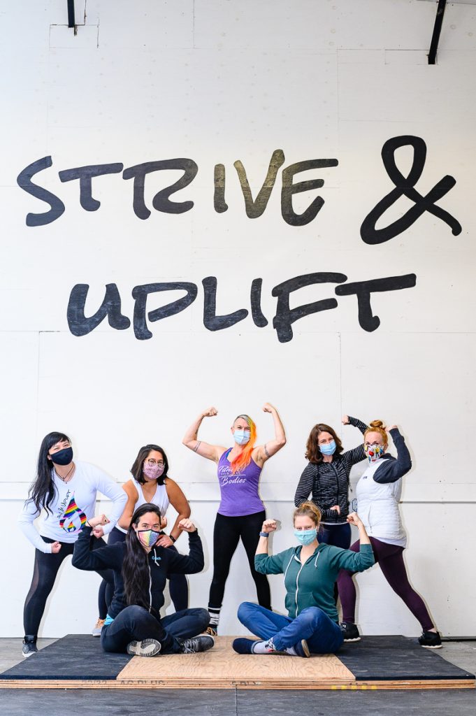 Strive & Uplift coaches, wearing masks, flex in front of a large mural reading "Strive & Uplift"